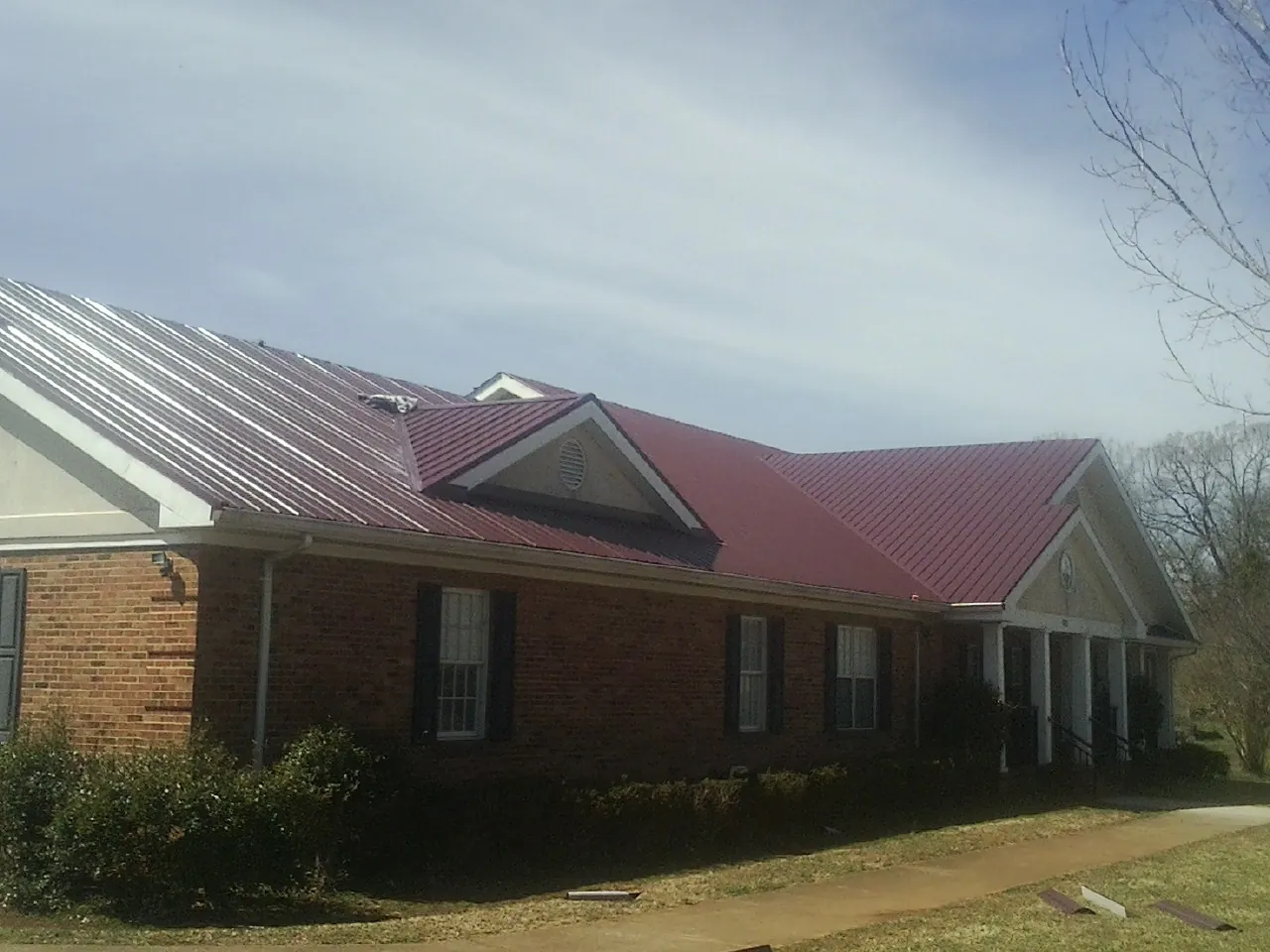 Red metal roof with gabled entries on a long brick building, from a Hail Damage Roof Repair job in Yelm