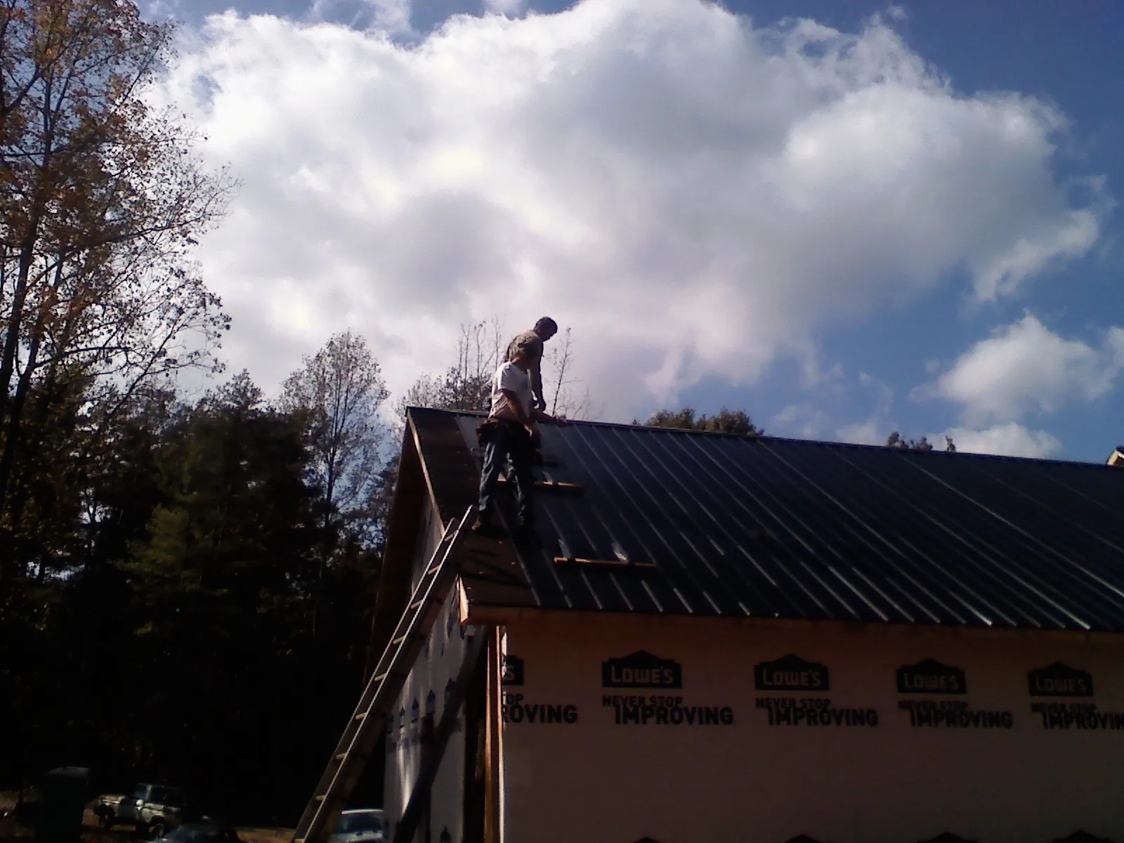 Roofer fastening dark metal panels high against a cloudy sky, from a Roof Inspection job in Yelm