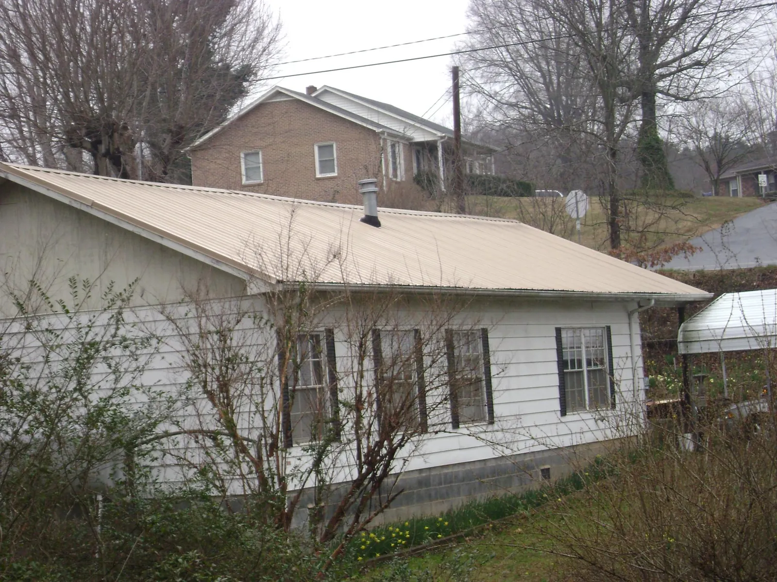 Tan metal roof on a white sided house set into a hillside — Commercial Roofing by Roofing Brothers in Yelm